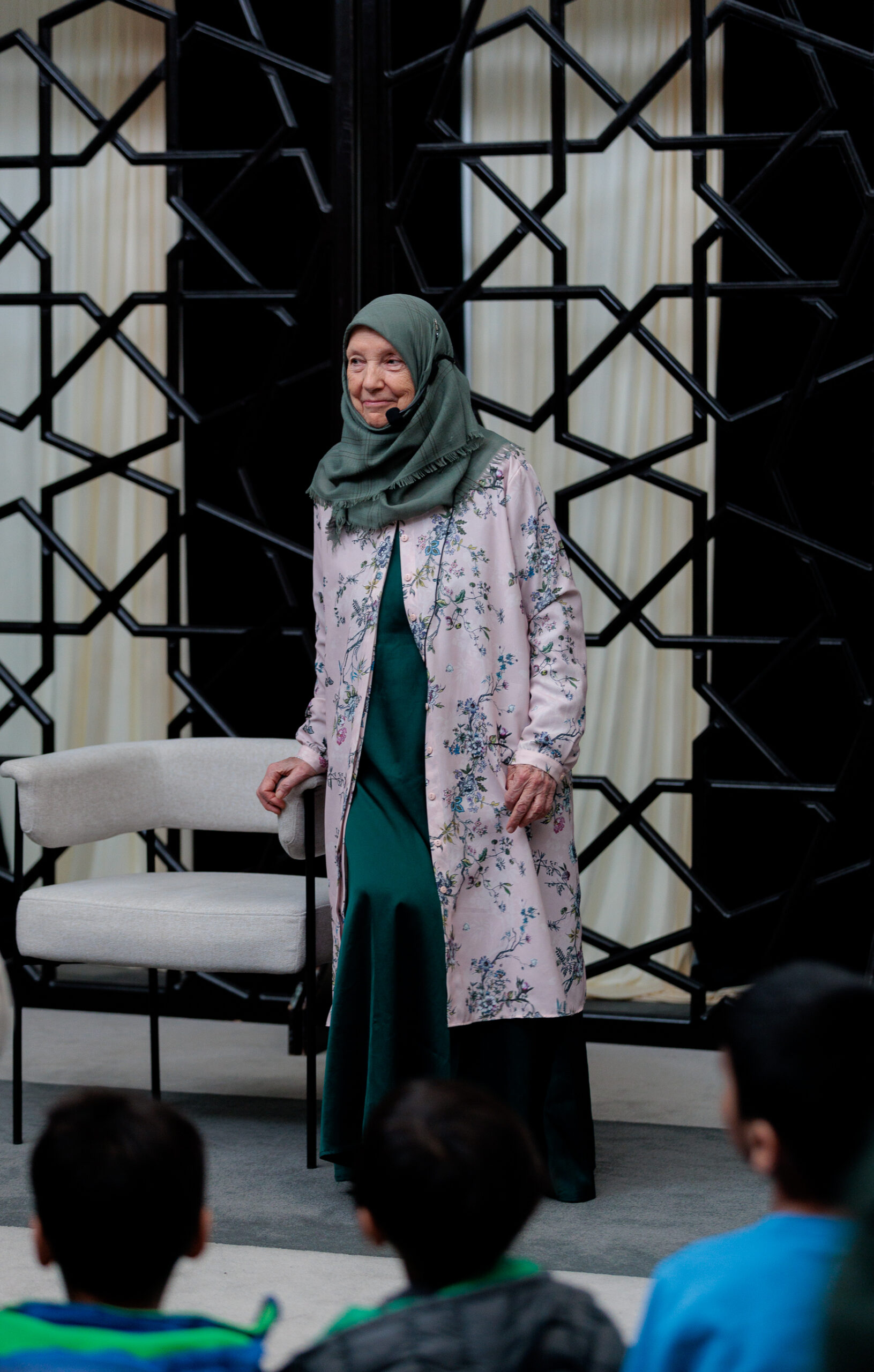 Mehded Maryam Sinclair wearing a headset microphone and standing before an audience of children at ISNA